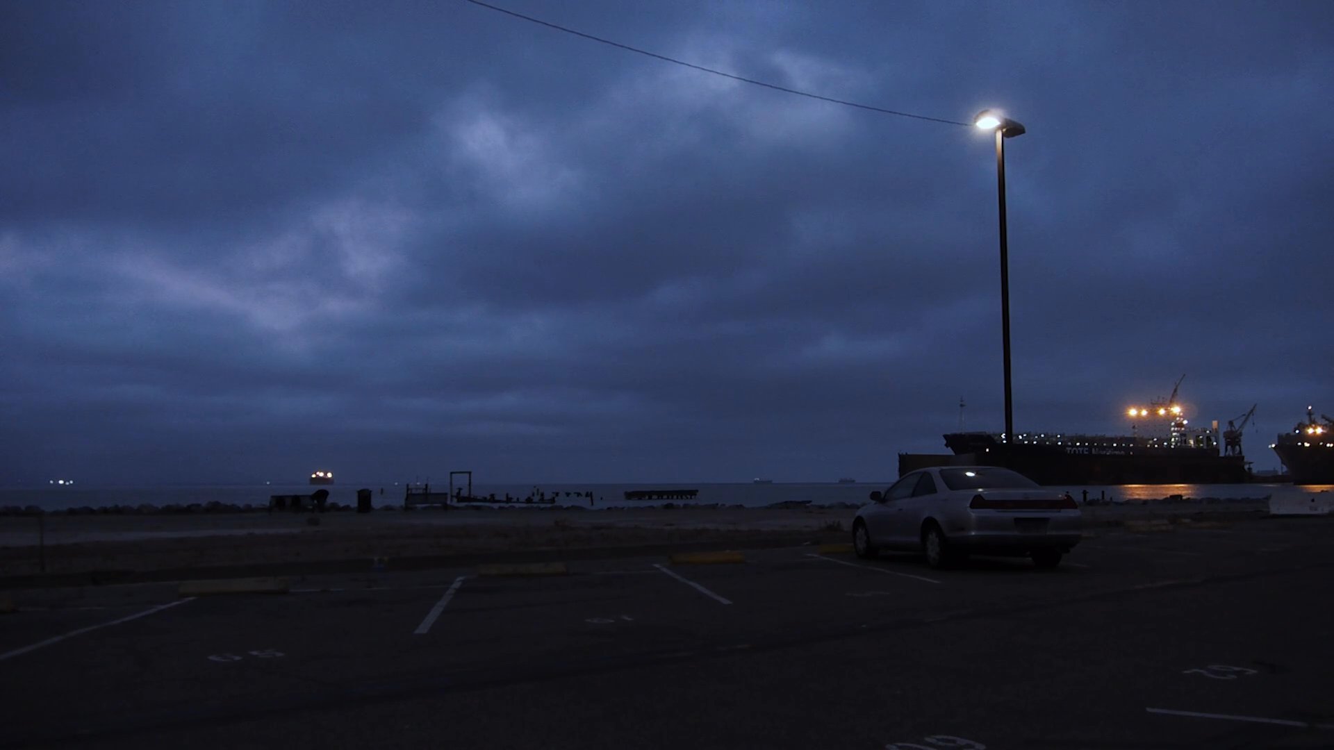 A woman exits an interior space at twilight and drives through a dark parking lot while engaged in a somber phone conversation.