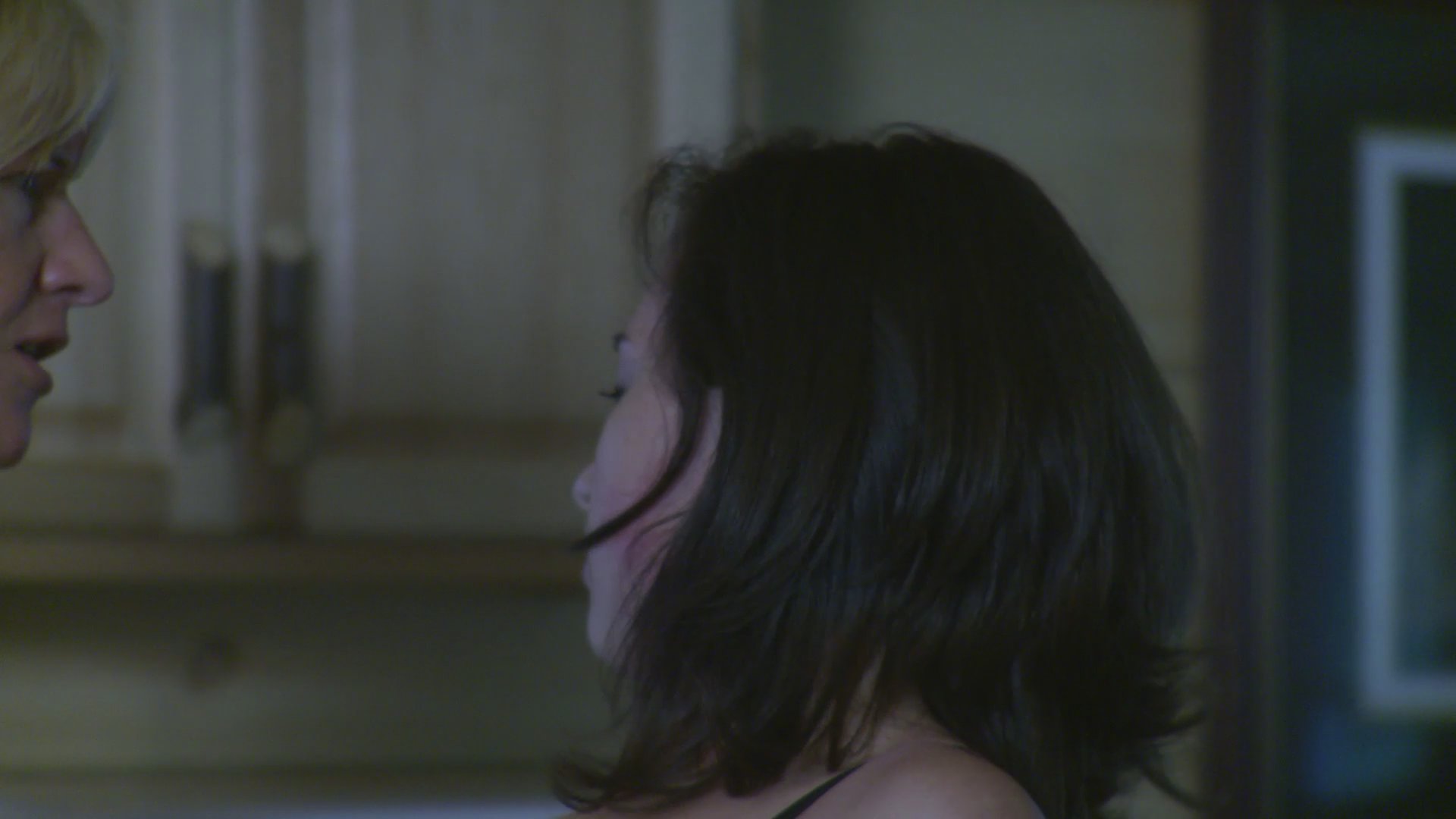 An older woman aggressively confronts and physically assaults a younger woman within a kitchen setting. The conflict escalates from an intense verbal exchange to the older woman seizing the younger woman by the throat.