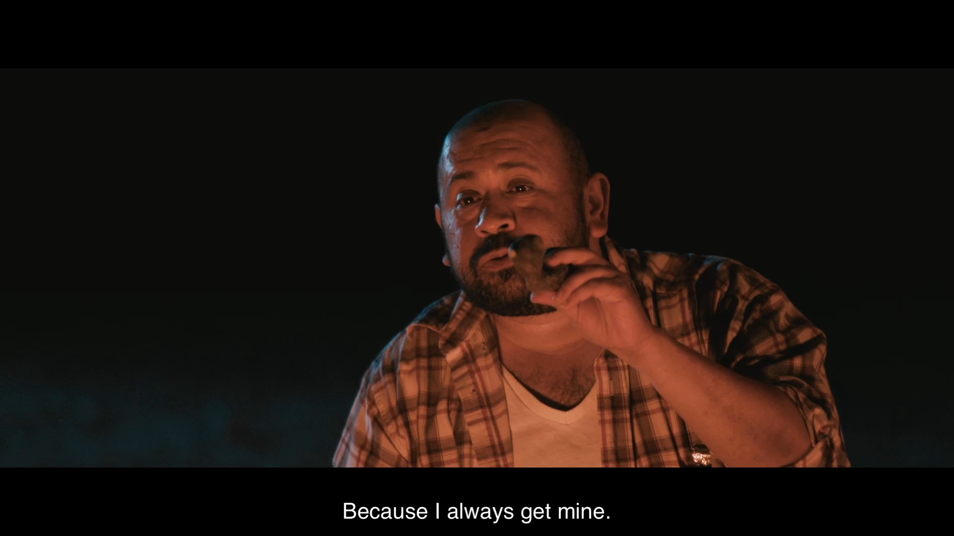 Two men sit by a campfire at night, sharing an intimate conversation about the metaphorical meaning of a roadrunner.