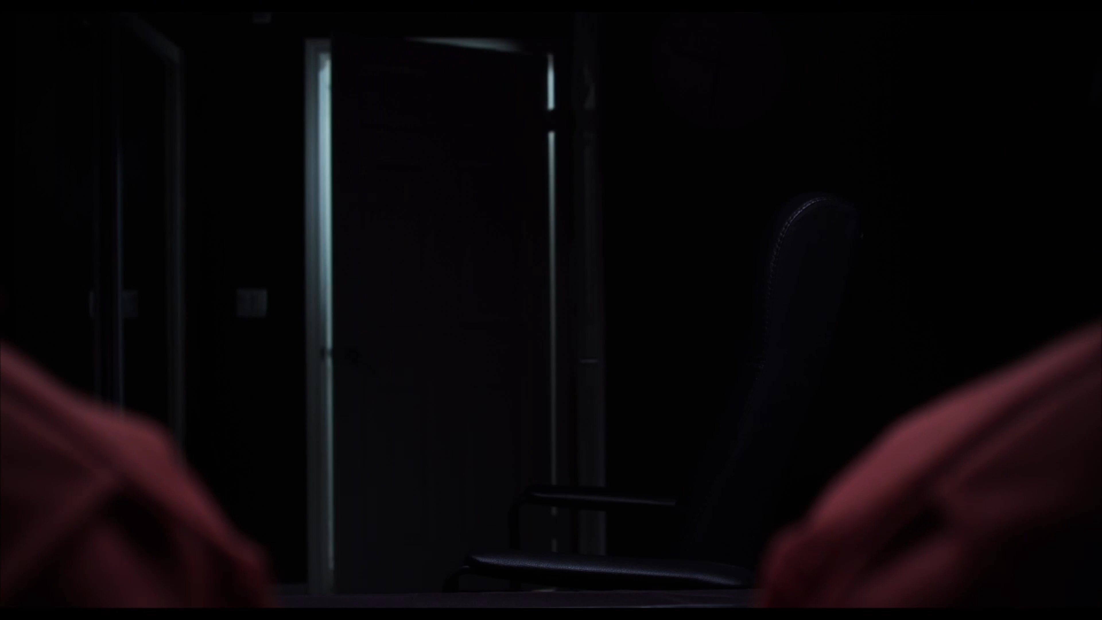 Two prisoners in orange jumpsuits engage in a tense conversation before a law enforcement officer enters the room to conduct an interrogation.