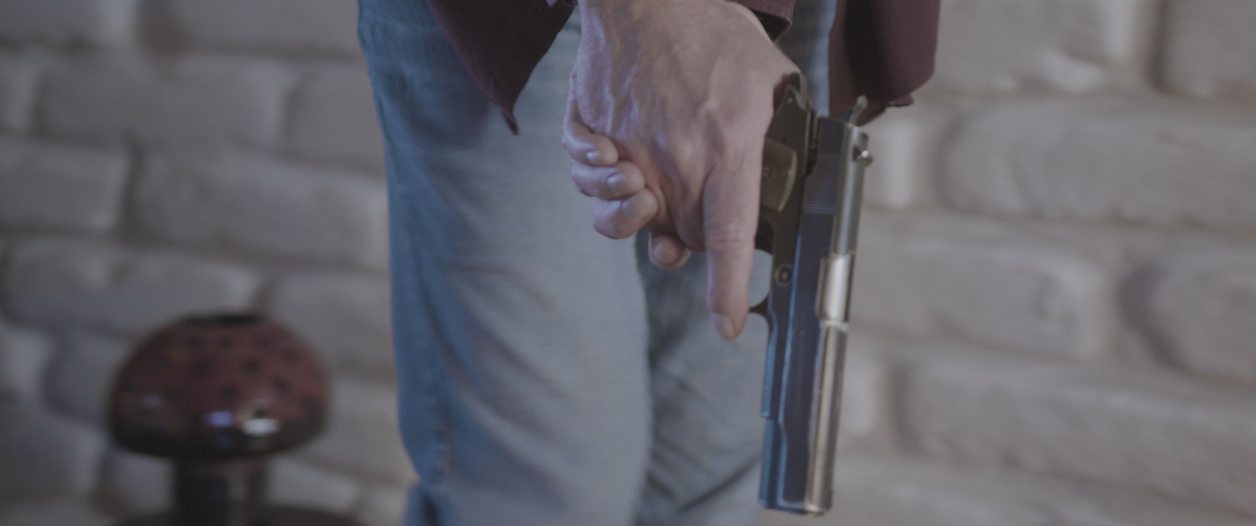 A woman wearing sunglasses peers through a small door hatch while an individual inside prepares a handgun in anticipation of a confrontation.