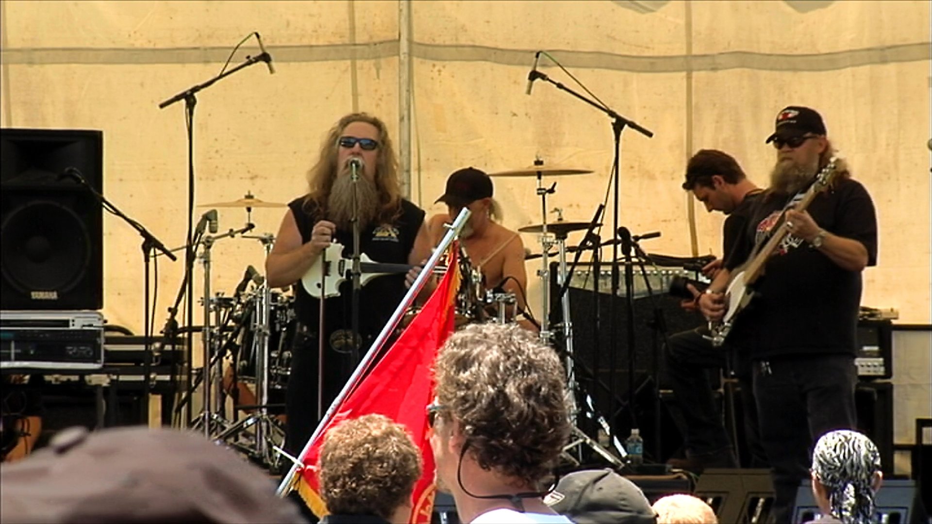 A band performs live music on an outdoor stage at a biker rally while attendees dance on the grass. The footage captures the high-energy atmosphere of the festival with focus on both the stage performers and the audience interaction.