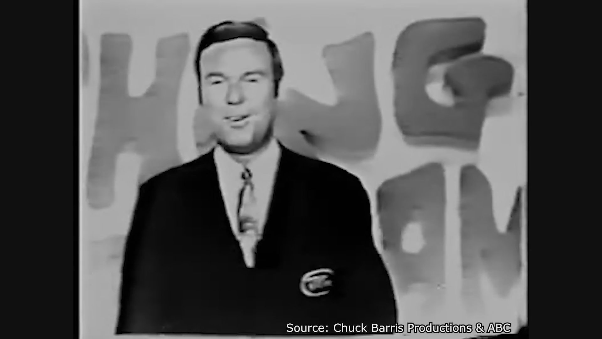 Host Jim Lange introduces the premiere of the television game show The Dating Game in 1965. The host walks onto a stage decorated with floral patterns and show branding to address the audience.