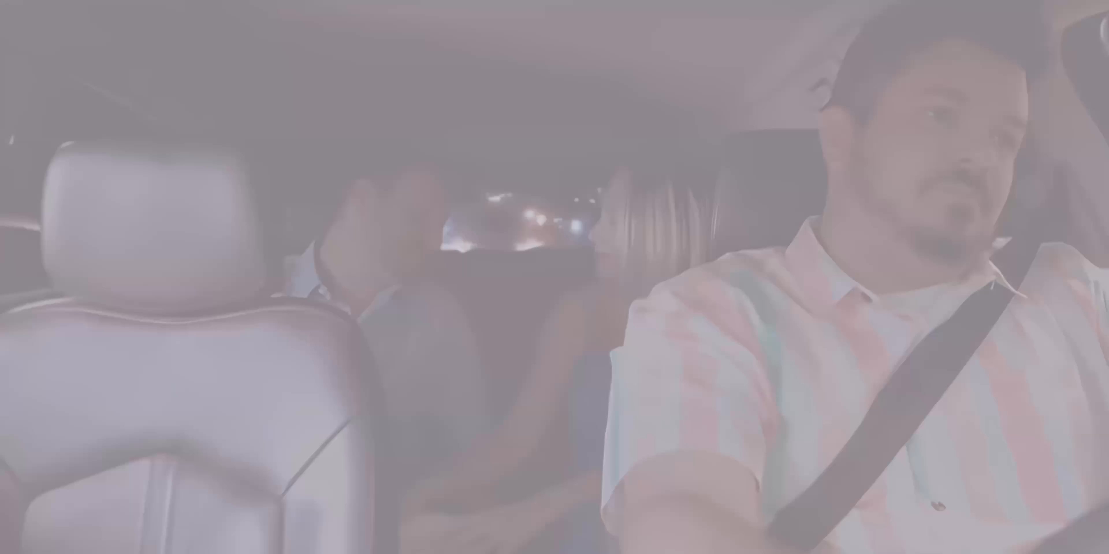 A driver transports passengers through a glowing city at night while engaged in conversation. The scene transitions between aerial urban views and the interior of the moving vehicle.