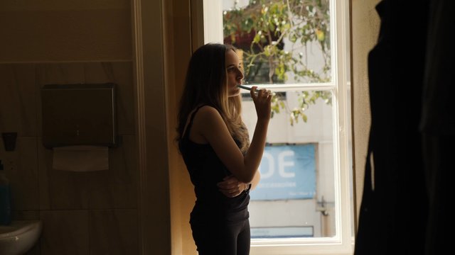 Girl brushing her teeth by a window