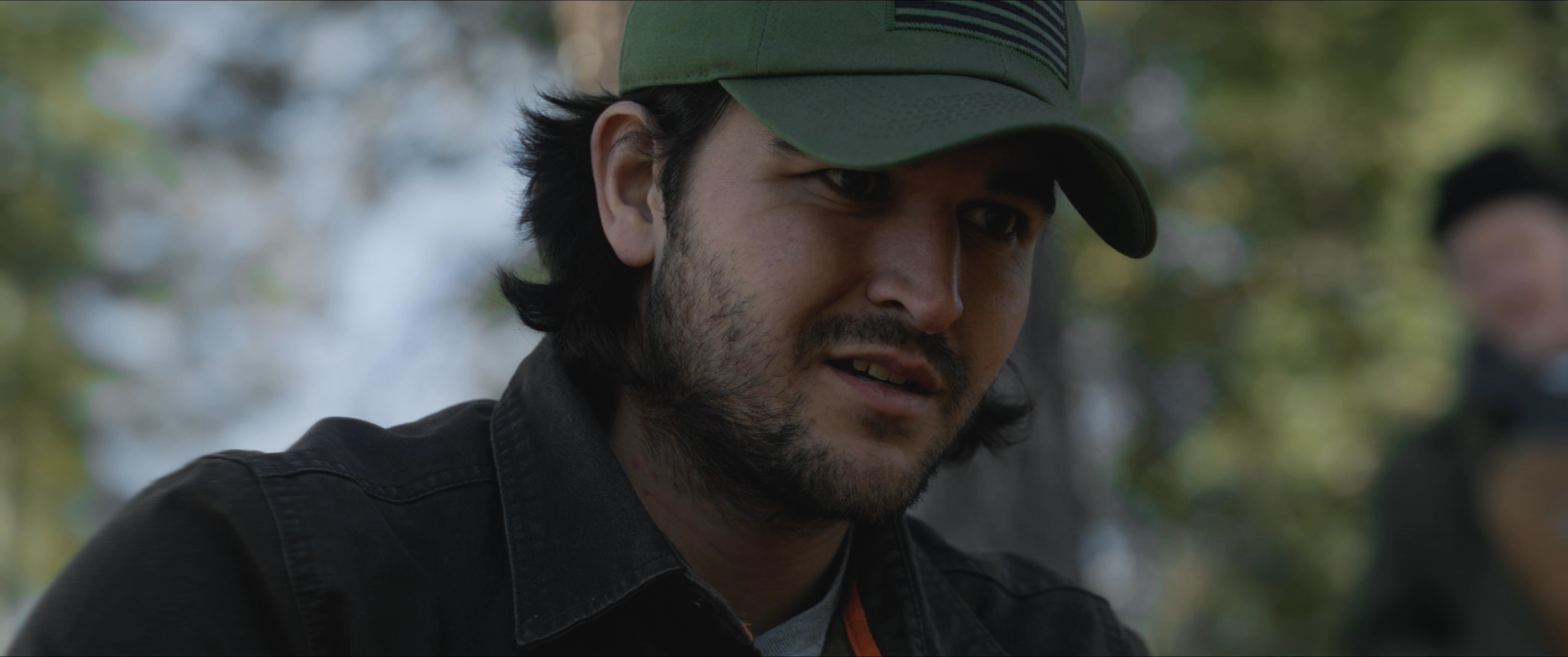 Two men engage in a serious conversation while situated within a dense forest setting.