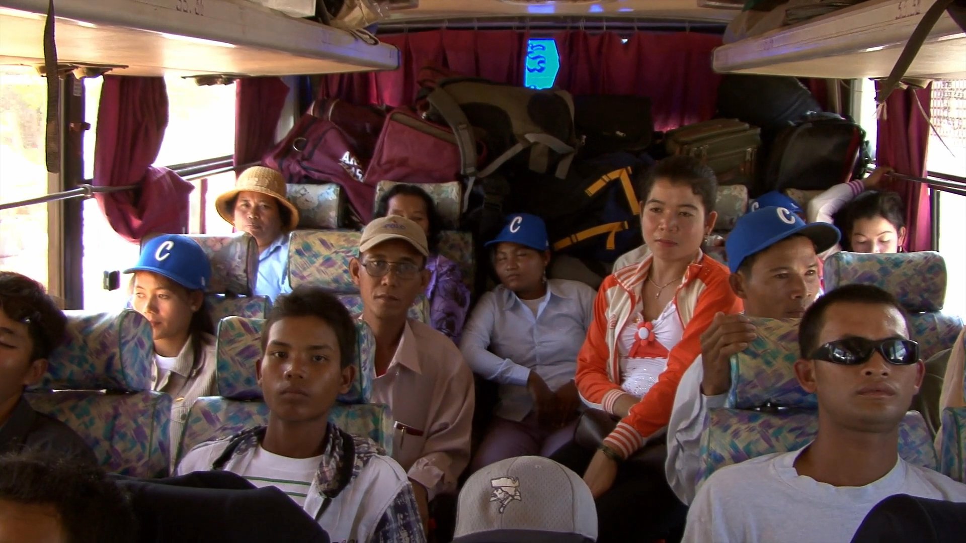 Travelers rest during a bus journey before arriving at the busy border crossing in Poipet, Cambodia, where passengers disembark to handle their luggage.