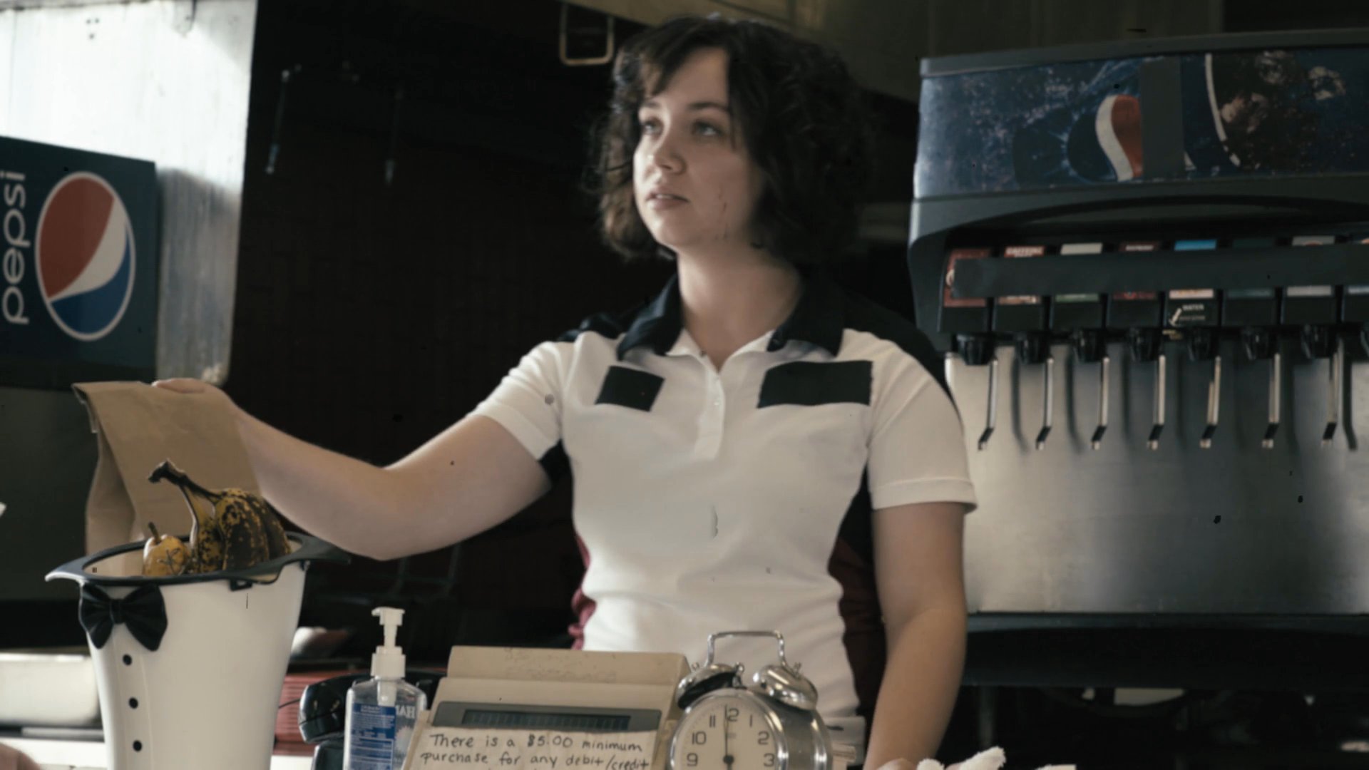 A man in a scarf completes a payment at a diner counter while interacting with the cashier. The scene captures the routine exchange between staff and patron in a casual dining environment.