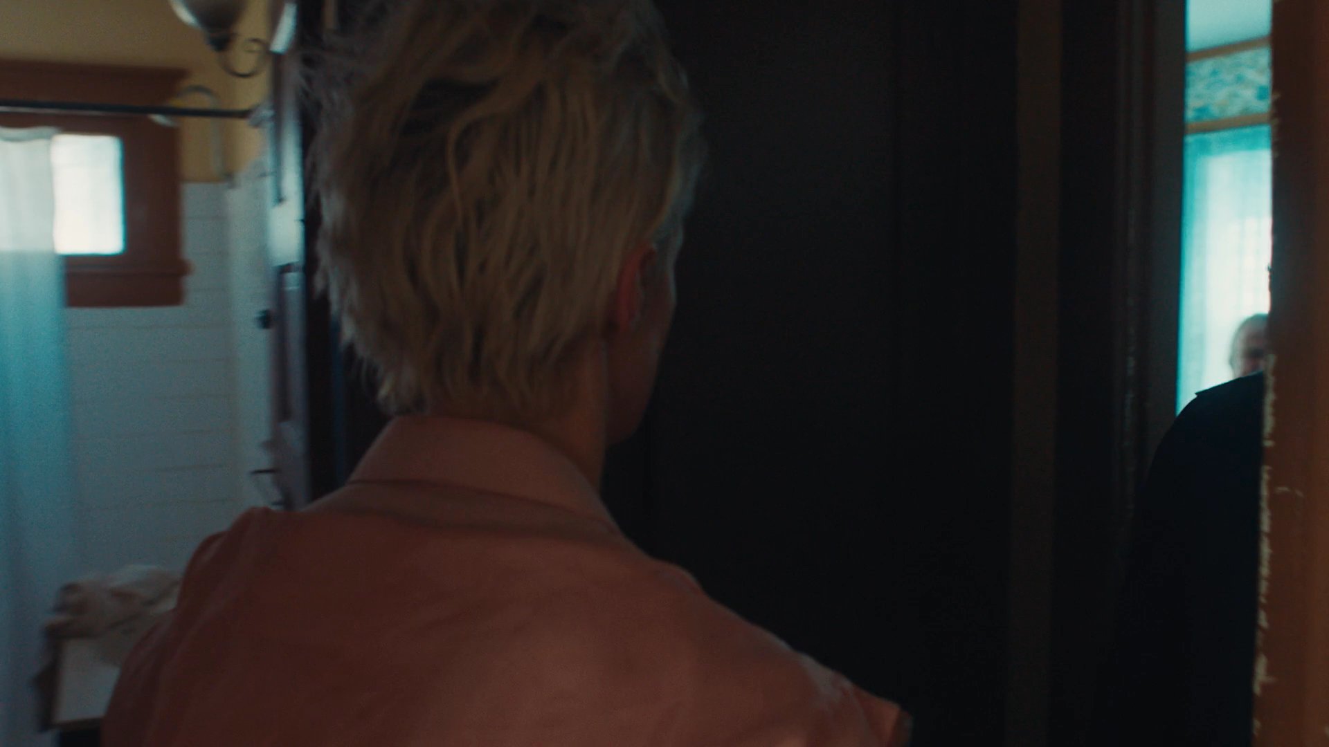 Two individuals share an intense, intimate moment before transitioning into a bedroom to confront an older man seated on the bed. The scene captures a shift from personal connection to a high-stakes, unsettling interpersonal standoff.