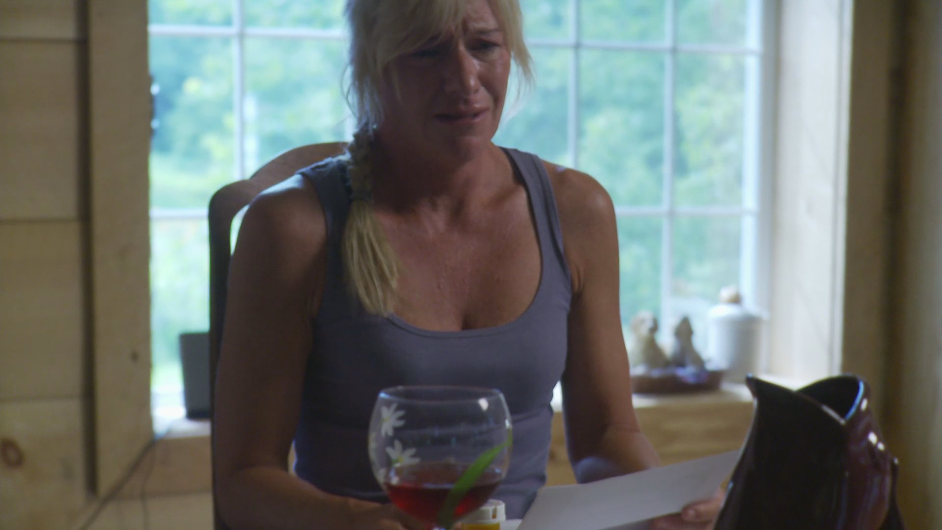 A woman experiences a moment of profound sadness while reading a document and drinking wine, later finding comfort in the presence of her golden retriever on her porch.