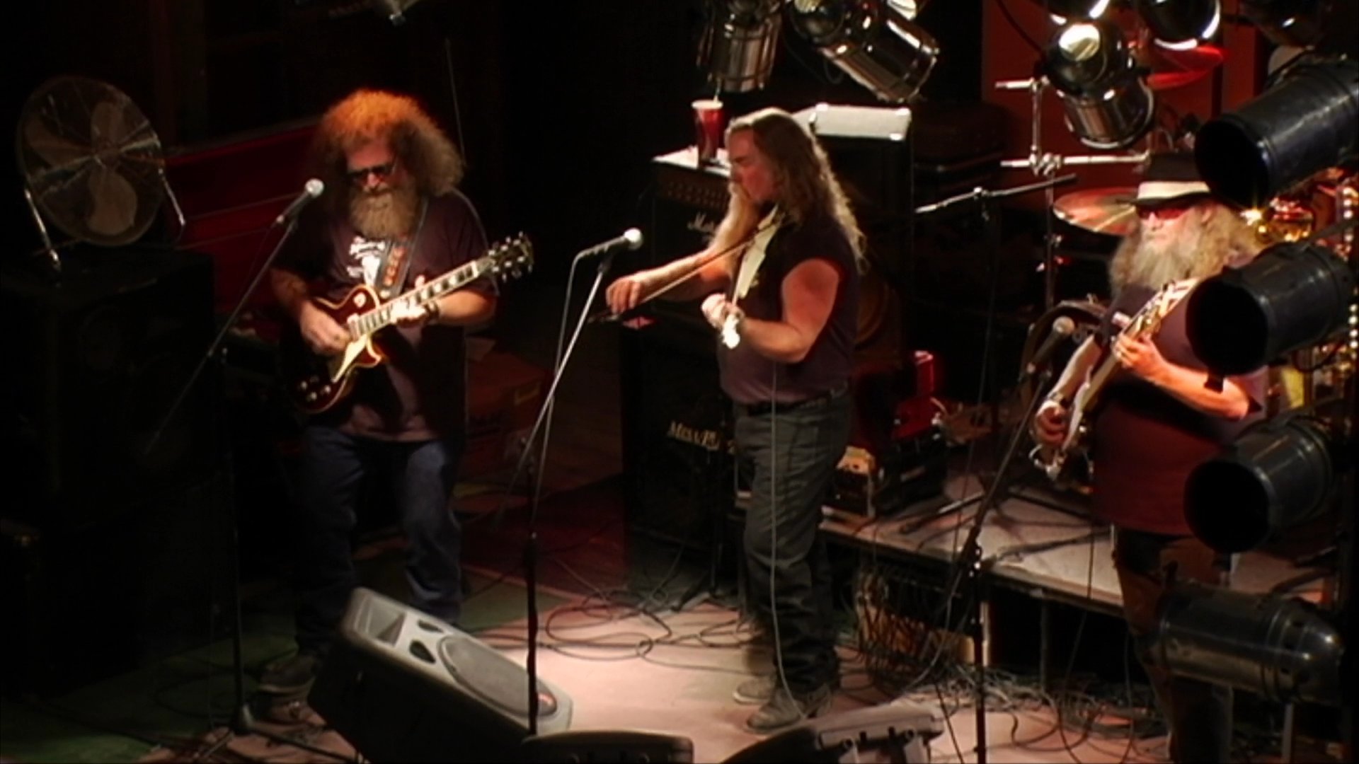 A musical duo featuring a guitarist and a violinist performs on a dimly lit stage at a venue. The performance highlights the musicians' interaction while playing their instruments for an audience.