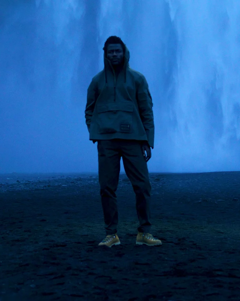 Man wearing AETHER + Mackintosh Field Anorak standing in front of waterfall in Iceland