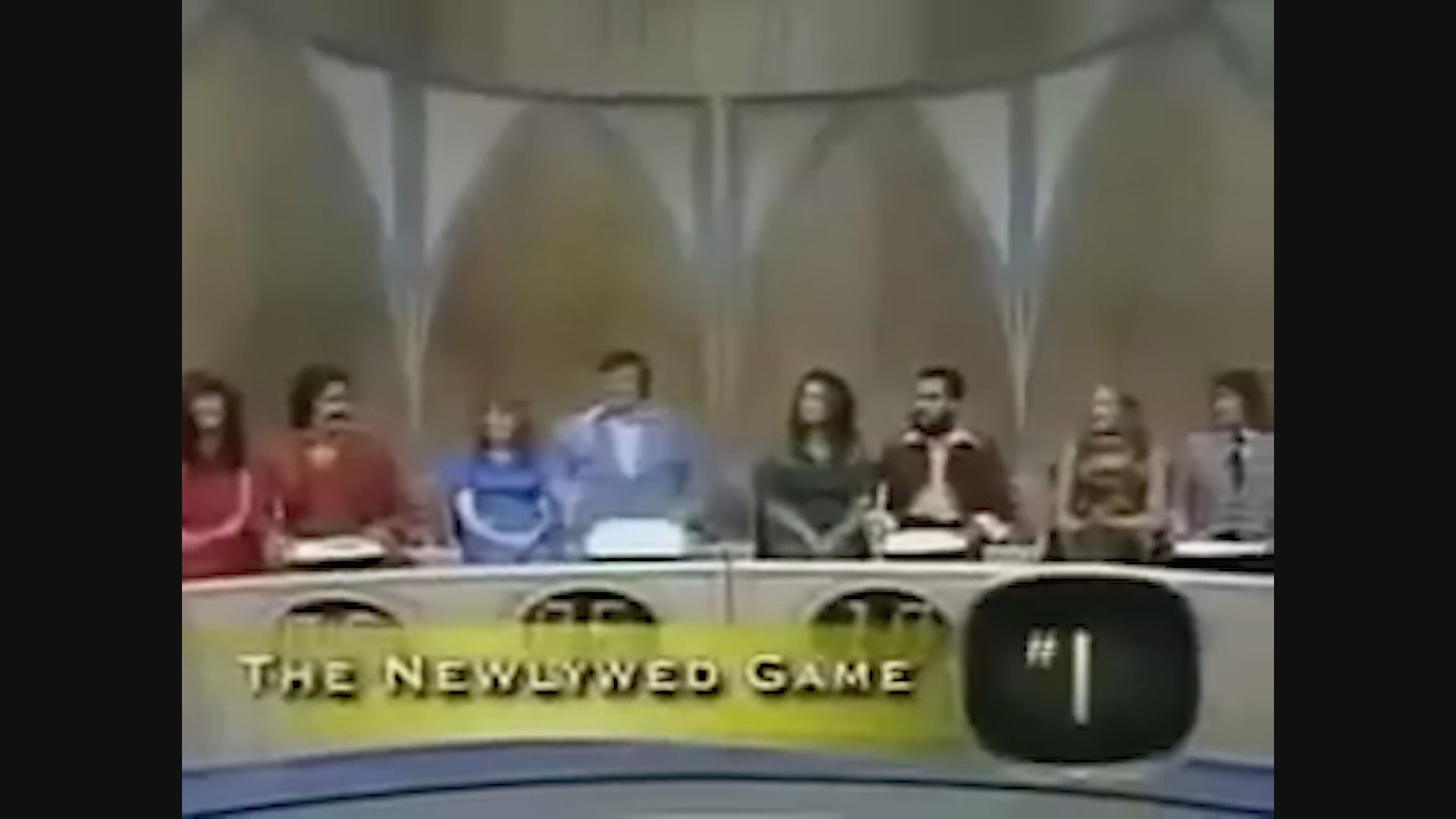 Host Bob Eubanks moderates a segment of The Newlywed Game as contestants display their scores at the studio desk.