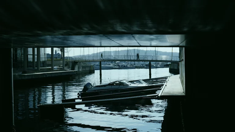 Two people walking across bridge over water with boats in Oslo