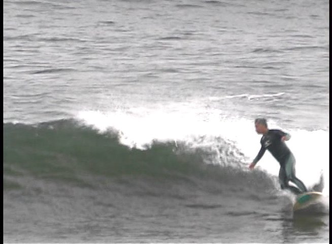 A surfer wearing a wetsuit rides a wave across the surface of the ocean. The individual demonstrates balance and control while maneuvering along the moving water.