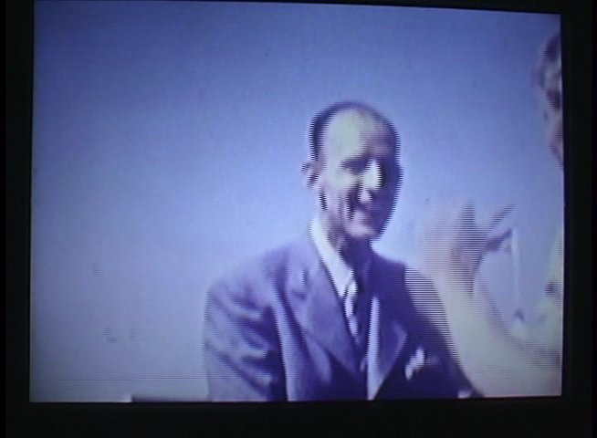 An elderly man discusses the historical significance of Duke Kahanamoku and his water carnivals, intercut with vintage footage of surfers at sea.