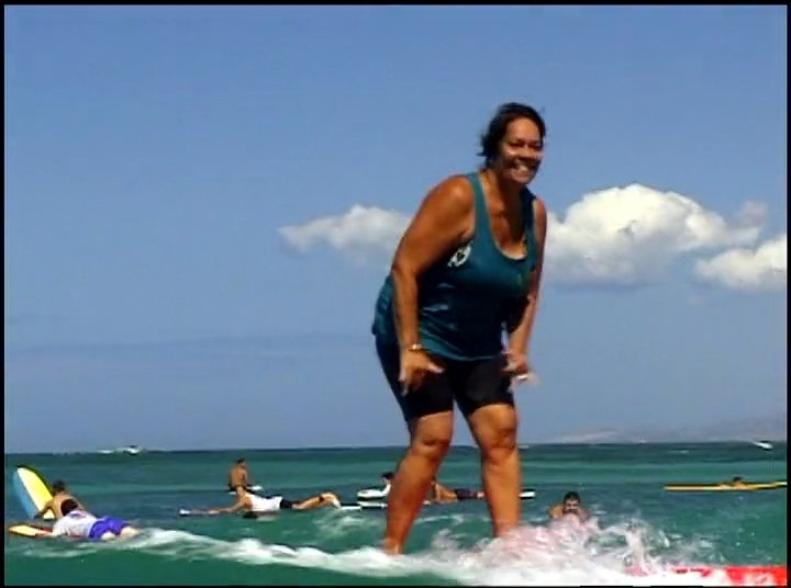 Individuals enjoy surfing on gentle ocean waves under a clear blue sky in a tropical coastal environment.