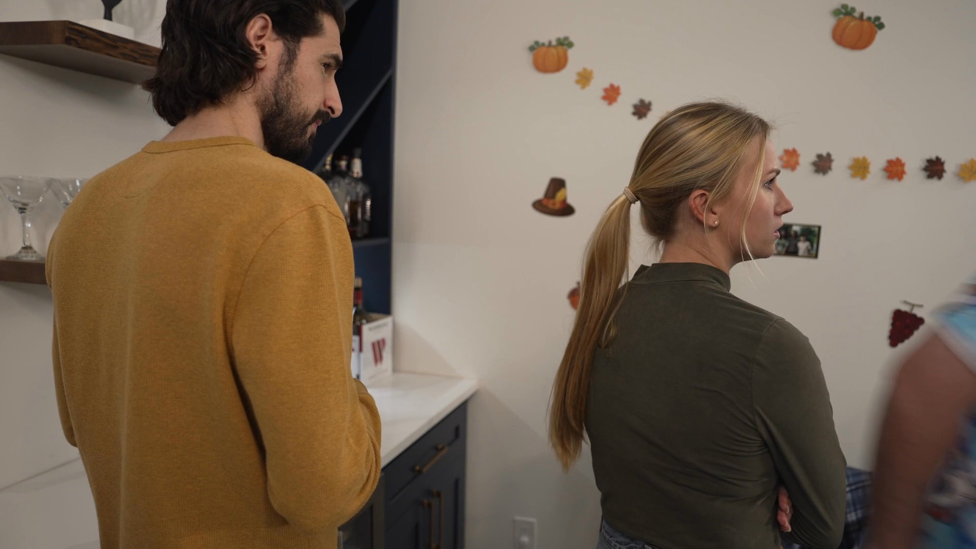 Friends and family socialize during a casual Thanksgiving celebration, transitioning from kitchen conversation to a shared meal at a decorated dining table.