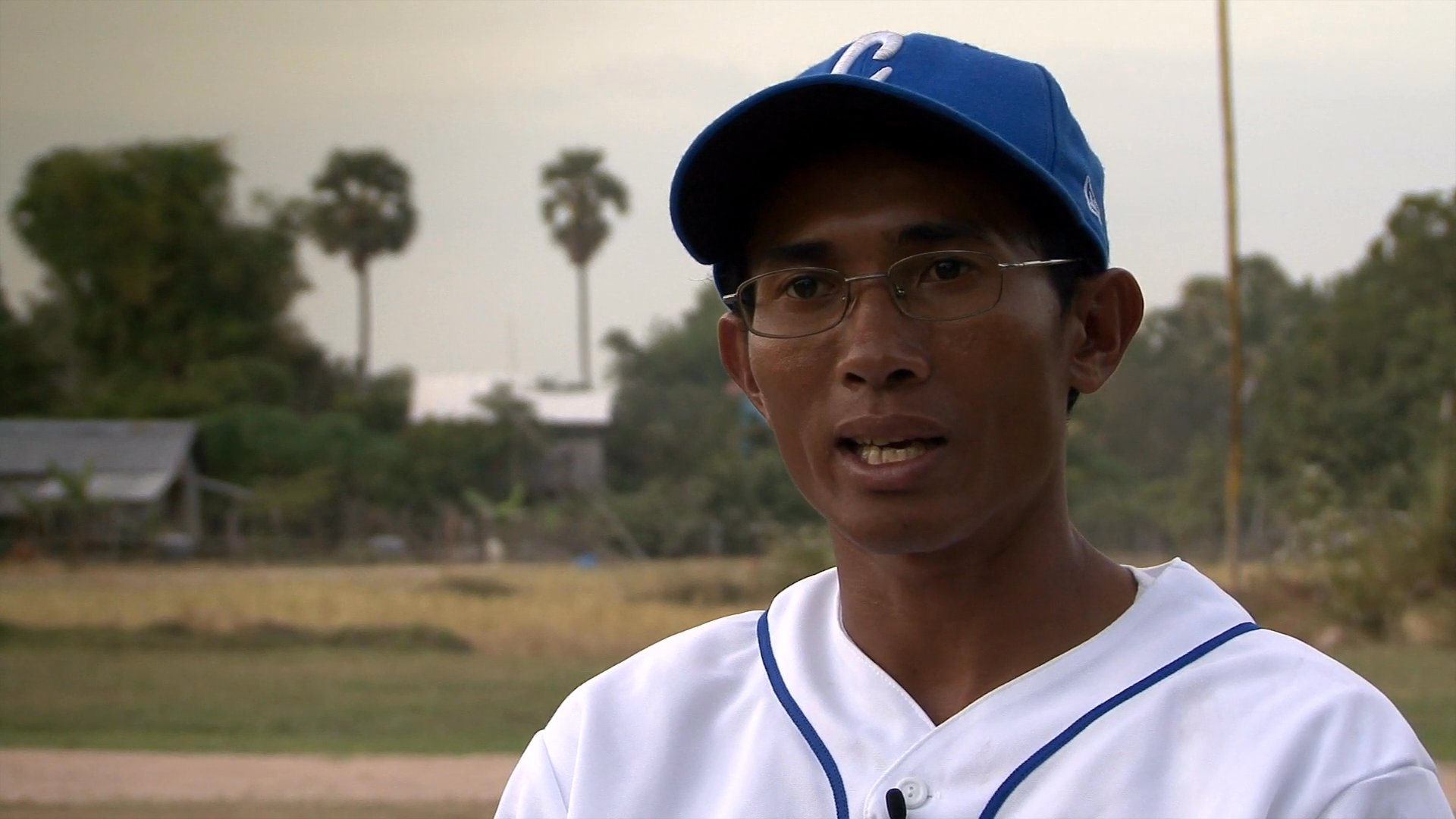 A man in a baseball cap shares personal reflections and historical accounts of Cambodia, contrasted against archival footage of historical military movements.