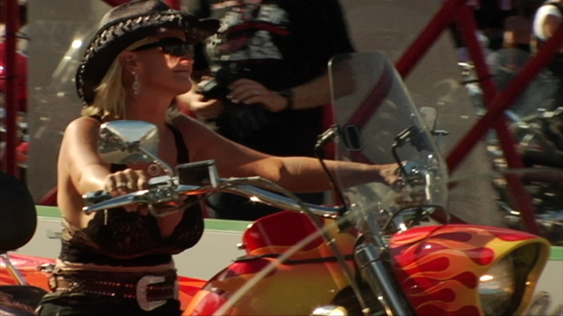 Participants celebrate and ride motorcycles during the Sturgis Motorcycle Rally. The scene transitions from outdoor road riding to social activities inside a crowded, beer-sponsored saloon.