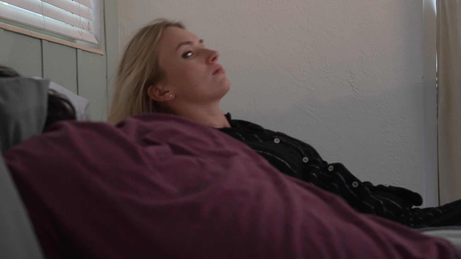 Two men watch a woman sleeping in a bedroom before she wakes up to discover blood on her face. The sequence shifts from voyeuristic observation to a moment of personal alarm.