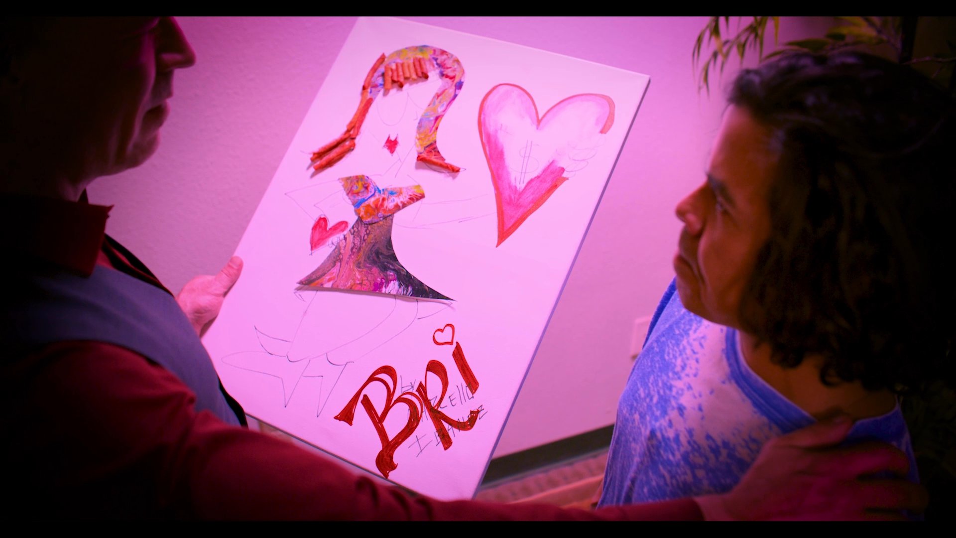 An adult male presents a piece of artwork featuring a heart and the name 'Bri' to a younger individual, initiating an intimate and supportive conversation.