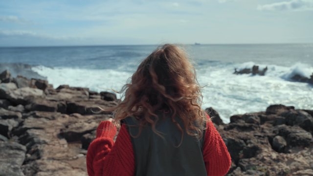 A girl tying her hair up while standing on a rocky shore