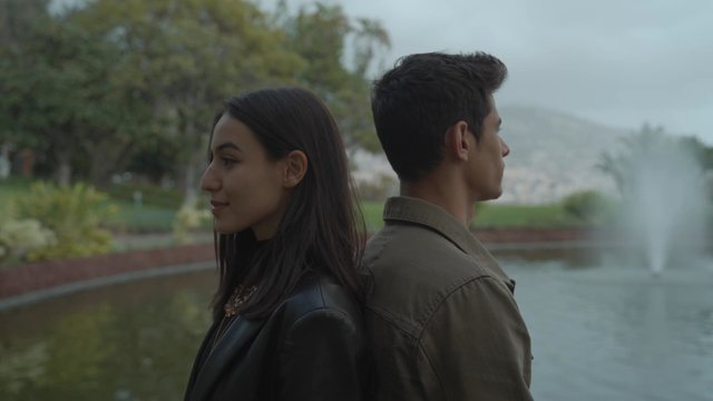 A couple is standing back to back in a park