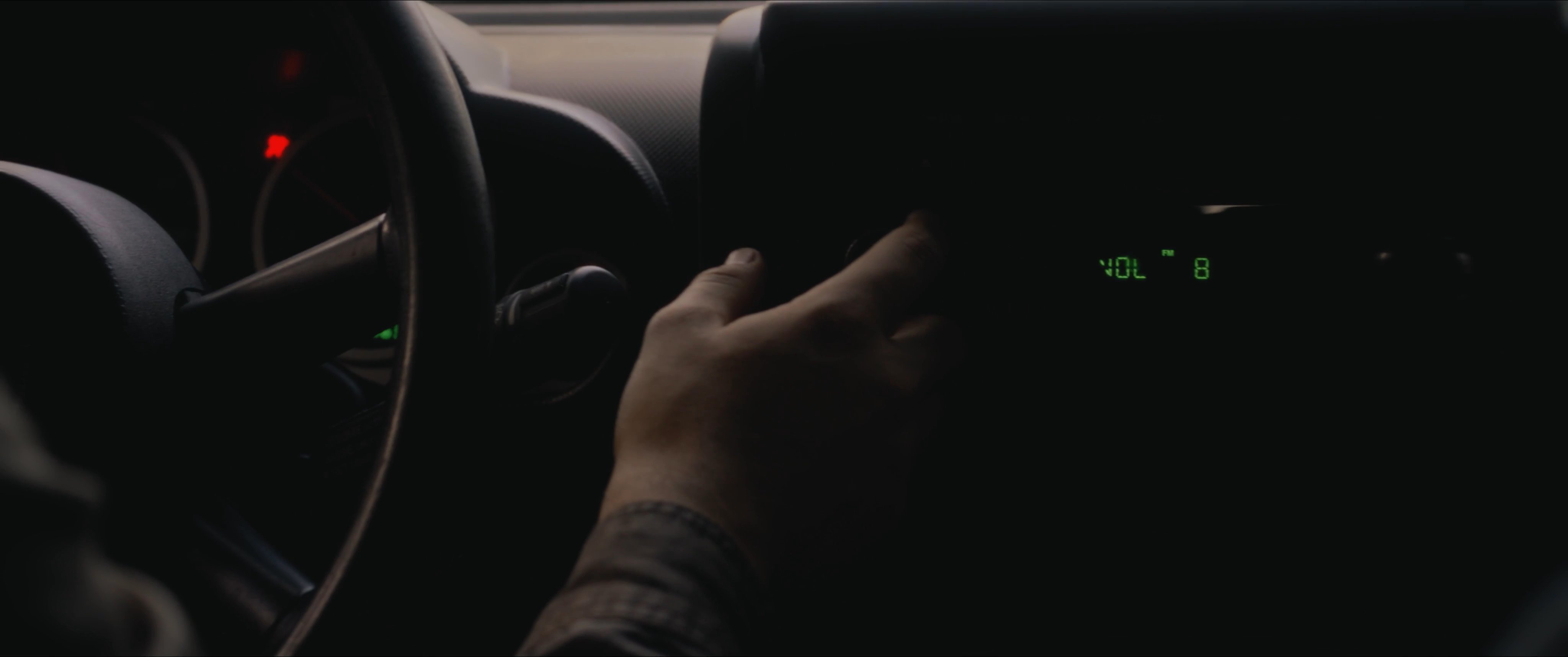 A driver navigates a winding road through a dense forest landscape during the golden hour. The perspective alternates between the driver's focused reflection in the mirror and the passing woodland scenery.