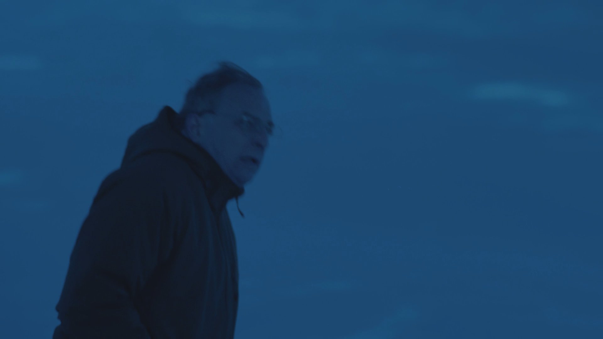 A man and woman engage in a tense argument beside a parked car on a desolate, snow-covered road.