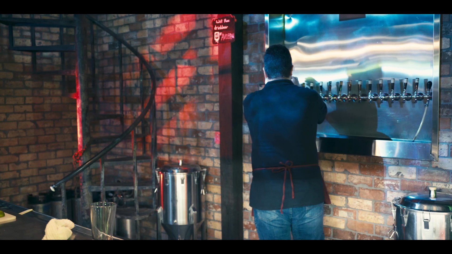 A professional bartender prepares a drink from a draft tap system and presents it to a customer at a bar counter. The two individuals engage in a brief conversation while the bartender finishes the service.