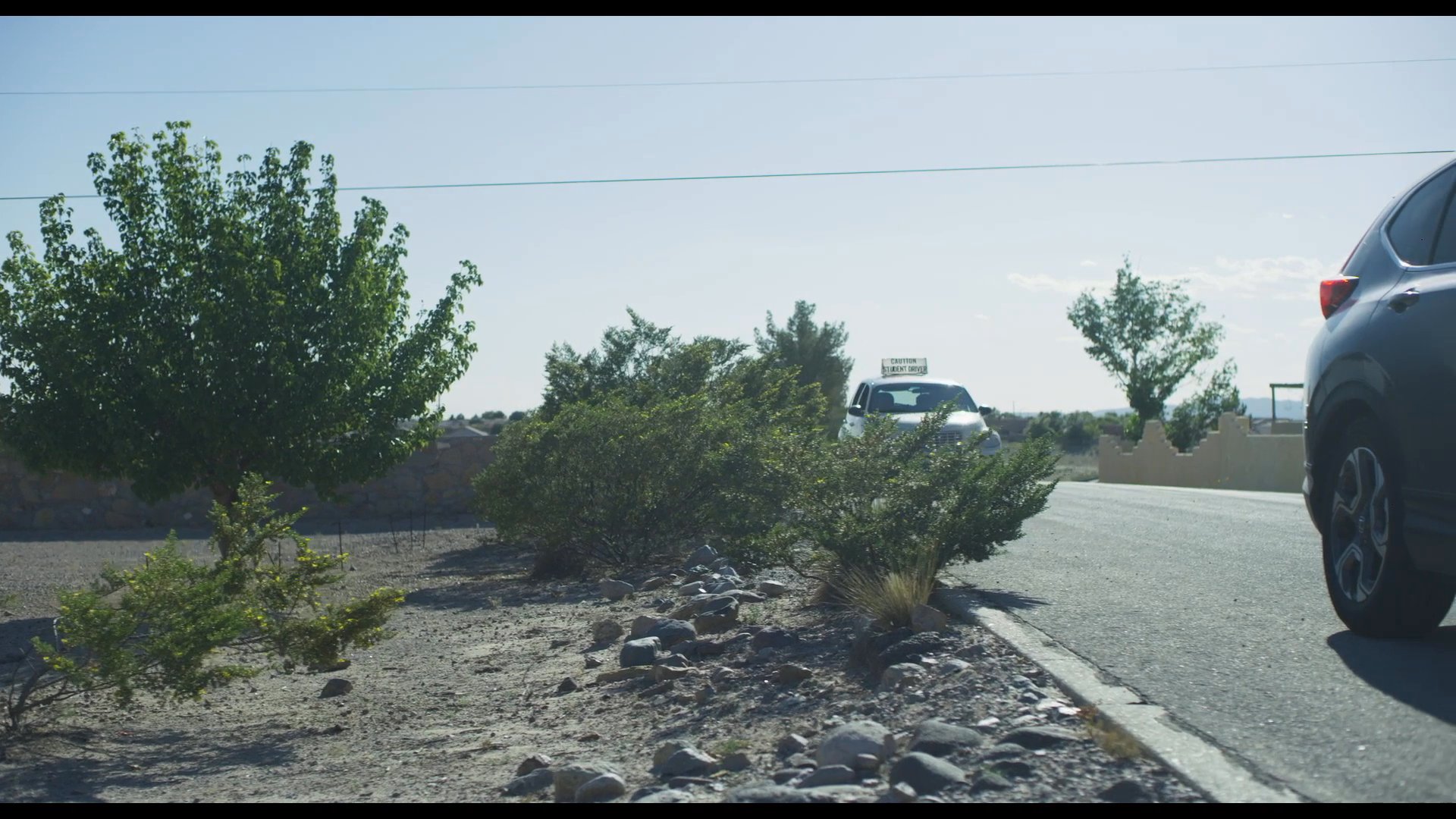A woman and a young man engage in a serious conversation while traveling in a car. The focus shifts from their interaction inside the vehicle to the roadside landscape as the car remains in motion.