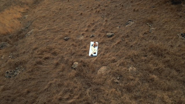 A man can't fall asleep on a bed in the middle of a field