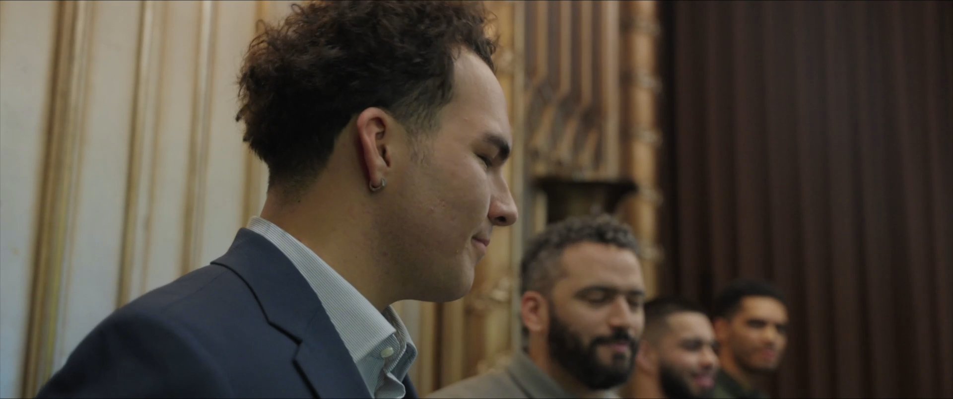 Individuals participate in a formal, structured proceeding within a wood-paneled courtroom environment. The attendees observe the speaker as he addresses the room, reflecting a serious and professional atmosphere.
