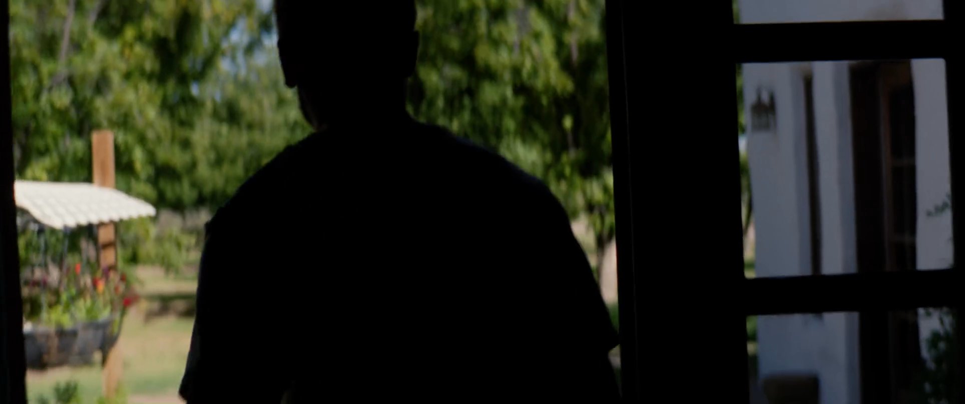 A man observes his grieving family at a loved one's bedside before walking alone into a sunlit orchard. The sequence captures a poignant moment of transition and personal reflection following a loss.