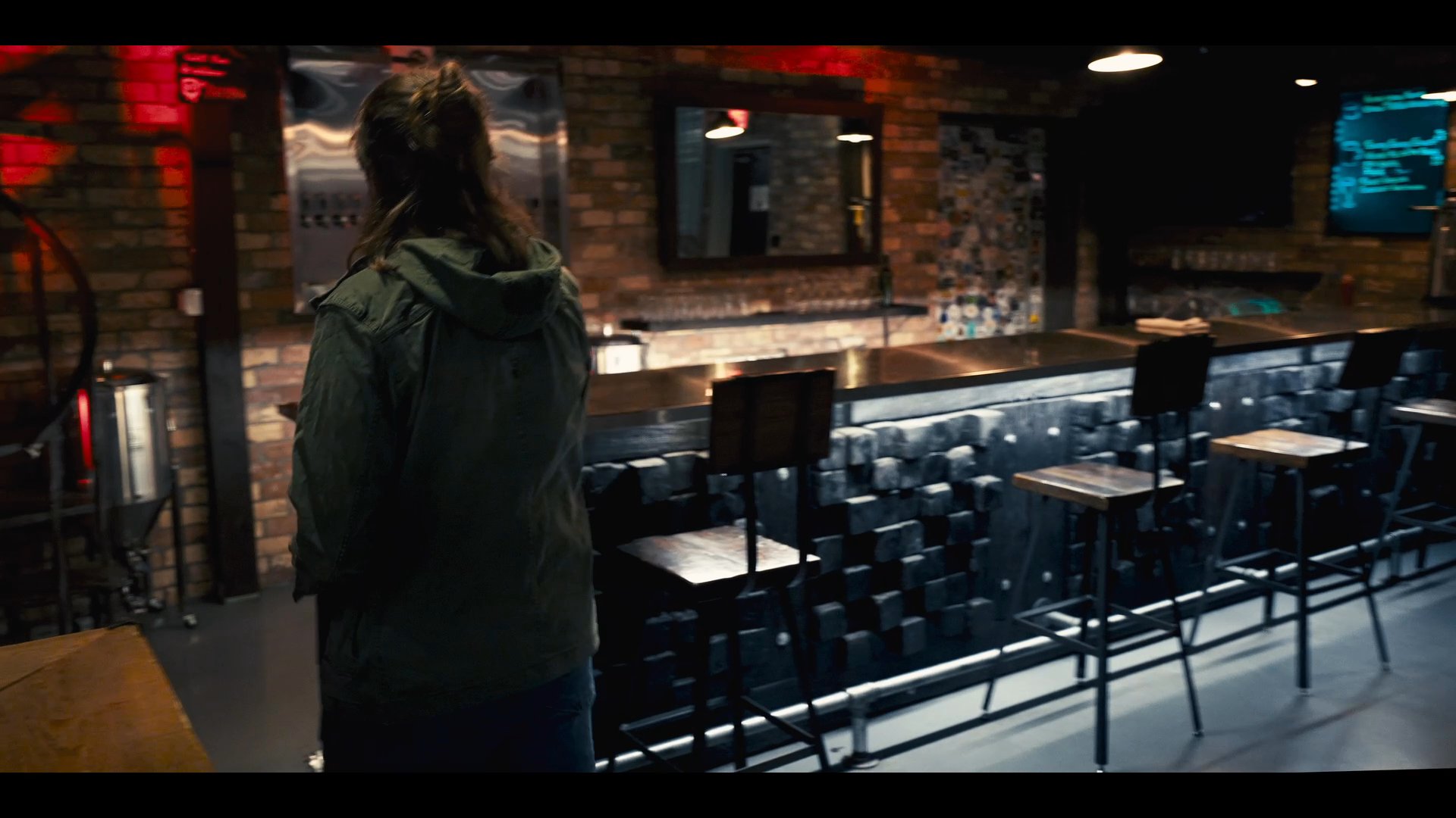 A man and woman engage in a tense conversation inside a dimly lit bar before the man abruptly turns and walks away from the counter.