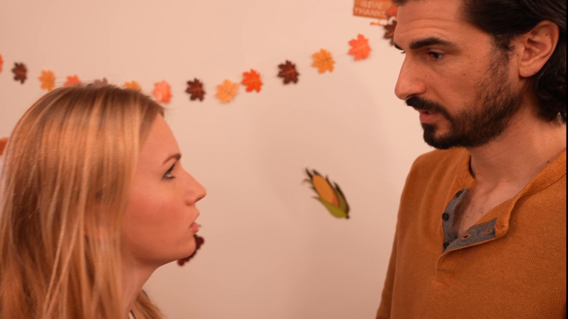 A woman and a man engage in a tense, confrontational conversation during a party while a third individual interrupts the interaction.