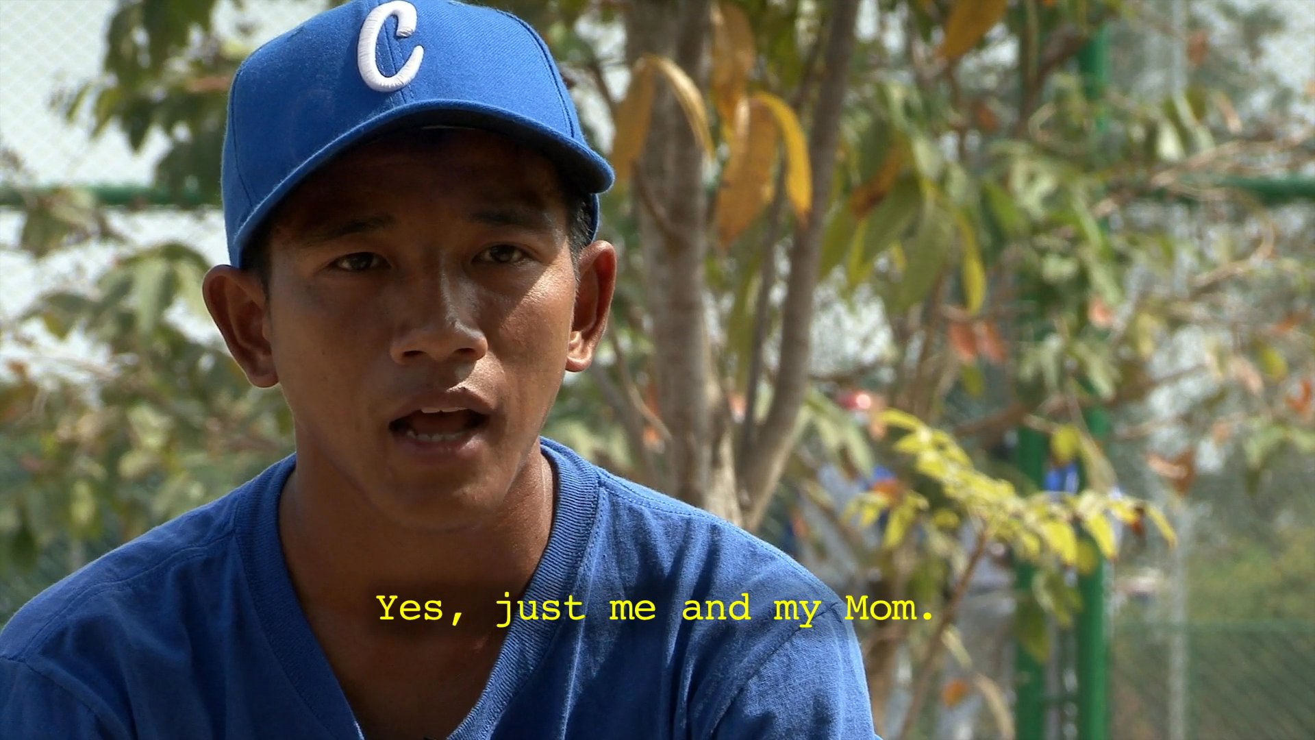 A young baseball player wearing a blue cap discusses his family background and early life experiences during an interview.