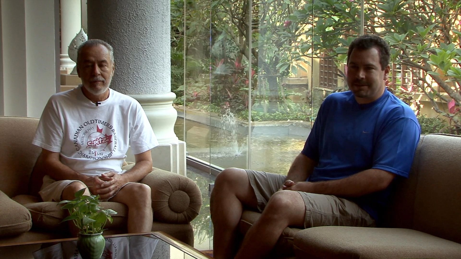Two men sit together on a sofa, engaging in an ongoing professional dialogue within a bright, indoor setting.