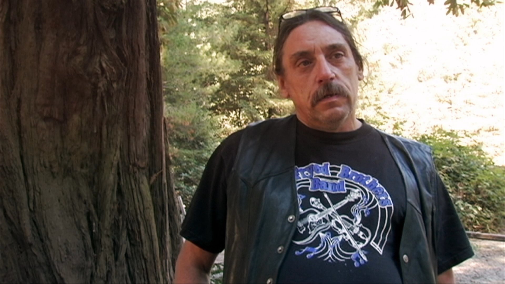 An individual participates in an outdoor interview, sharing personal insights while positioned in a wooded, natural environment.