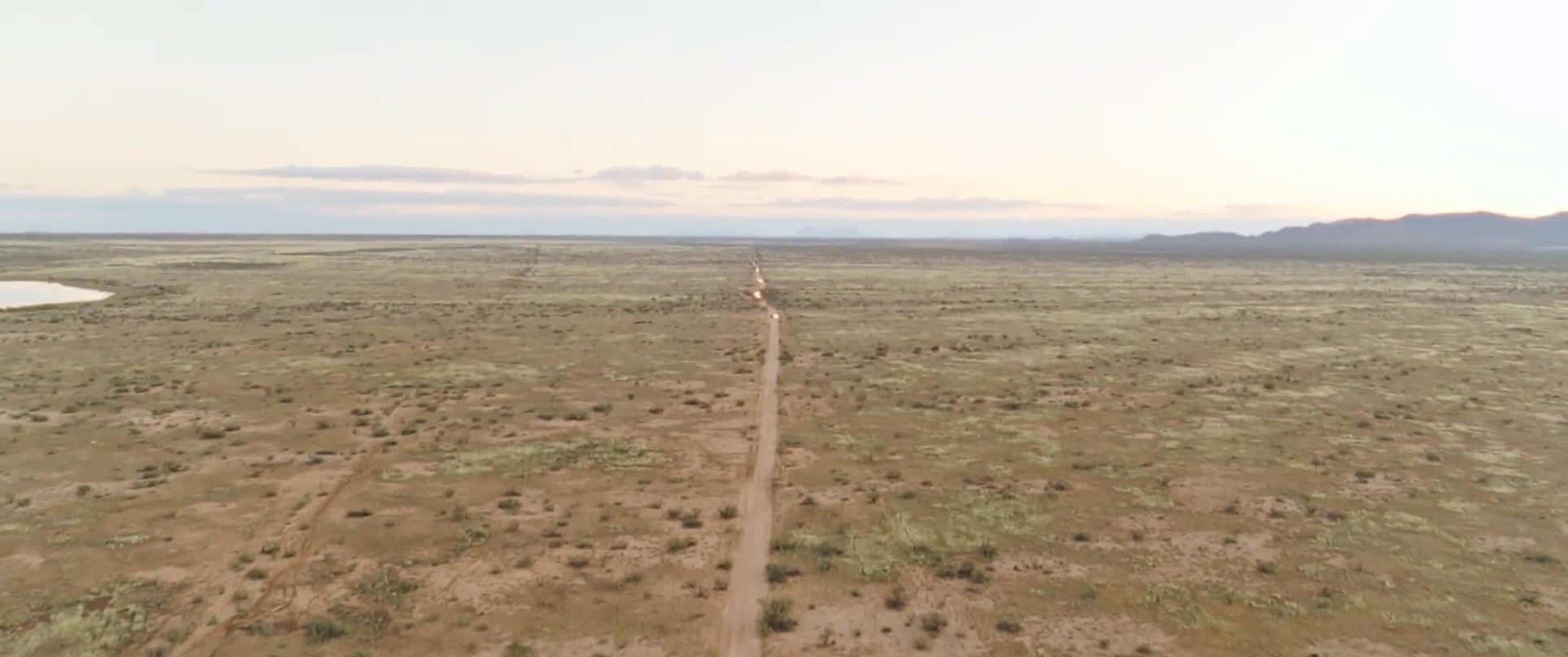 A rider travels across an expansive desert landscape on horseback before arriving at a remote ranch property where a vintage pickup truck is parked.