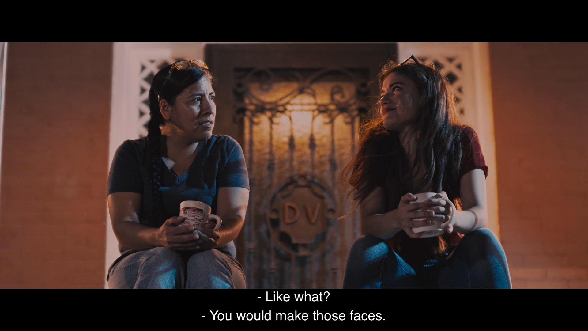 A mother and daughter engage in a personal conversation about past relationships and communication struggles. They sit together in a warm, dimly lit environment while sharing a moment of vulnerability.
