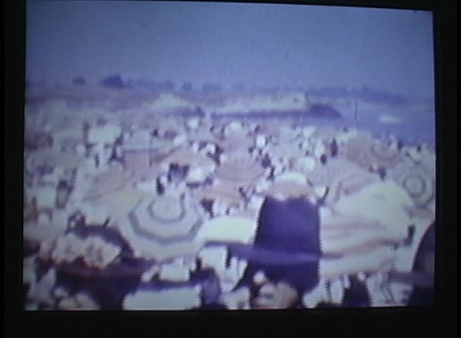 Historical footage captures a crowded seaside boardwalk during the 1930s, showcasing beachgoers relaxing under parasols and strolling along the wooden promenade.