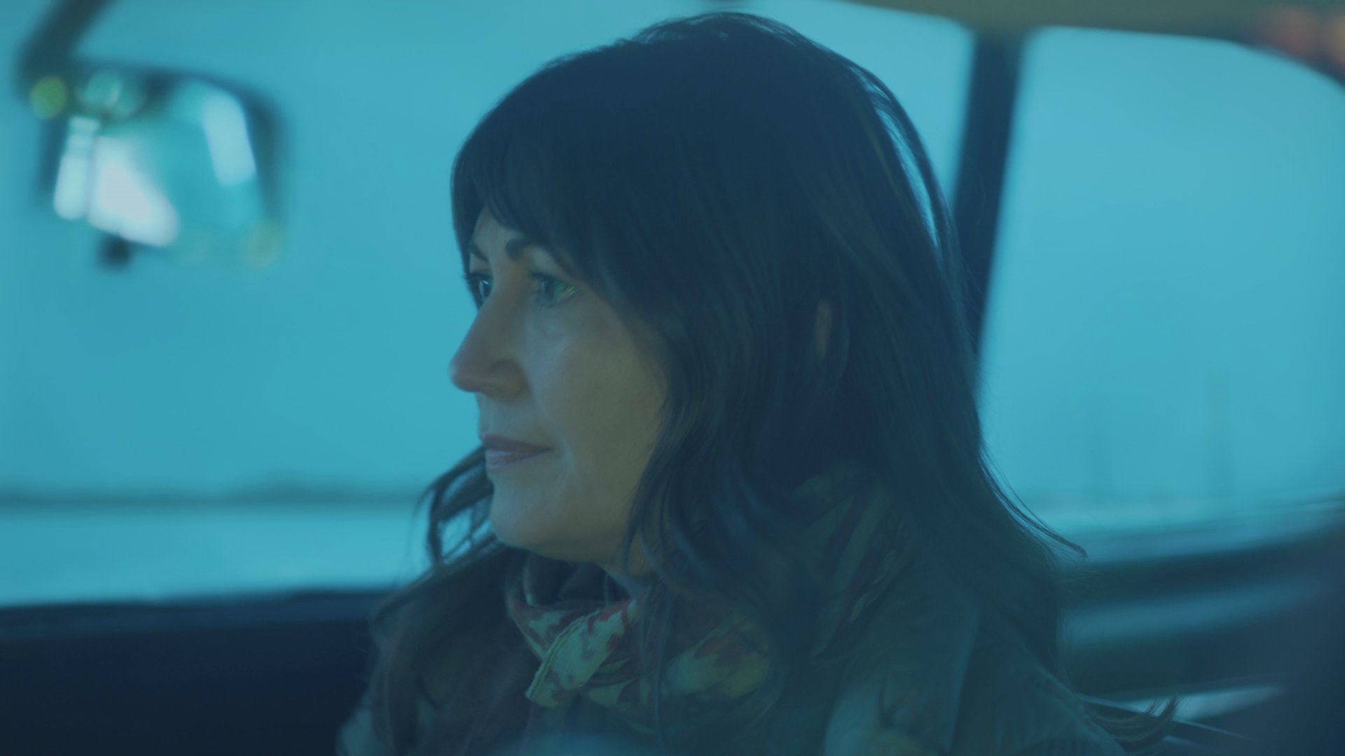 A man and a woman engage in a serious, quiet conversation while sitting inside a parked vehicle during evening hours.