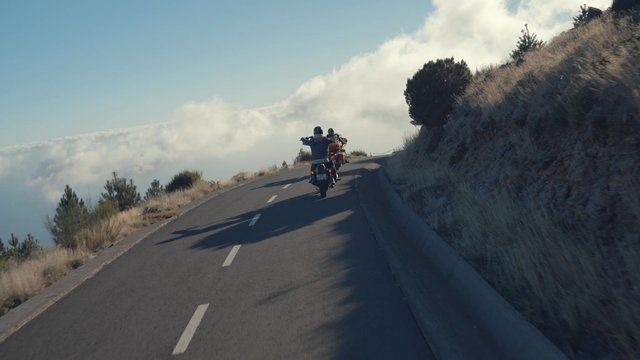 Two bikers are driving through an uphill curve in the road