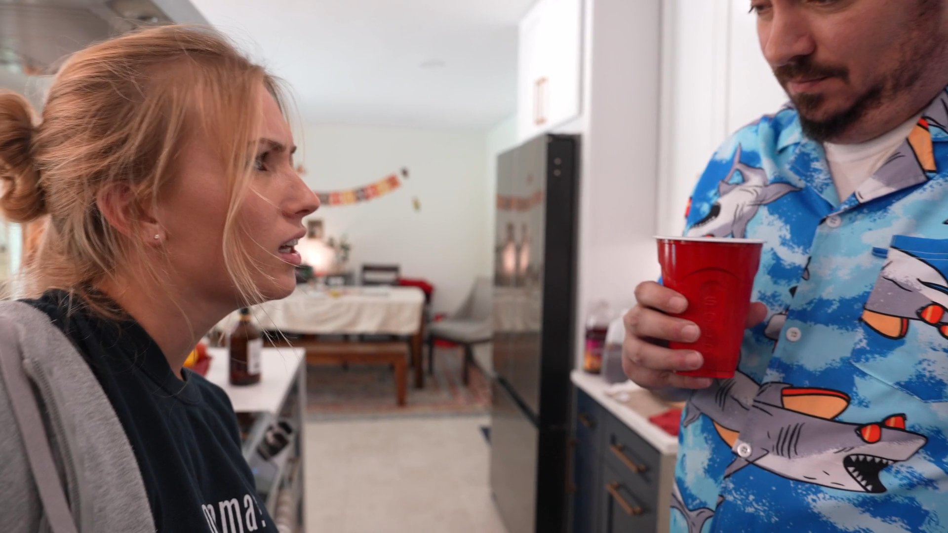 A woman and a man engage in an intense, animated conversation in a residential kitchen setting. The interaction displays clear signs of interpersonal tension and disagreement as they face one another.