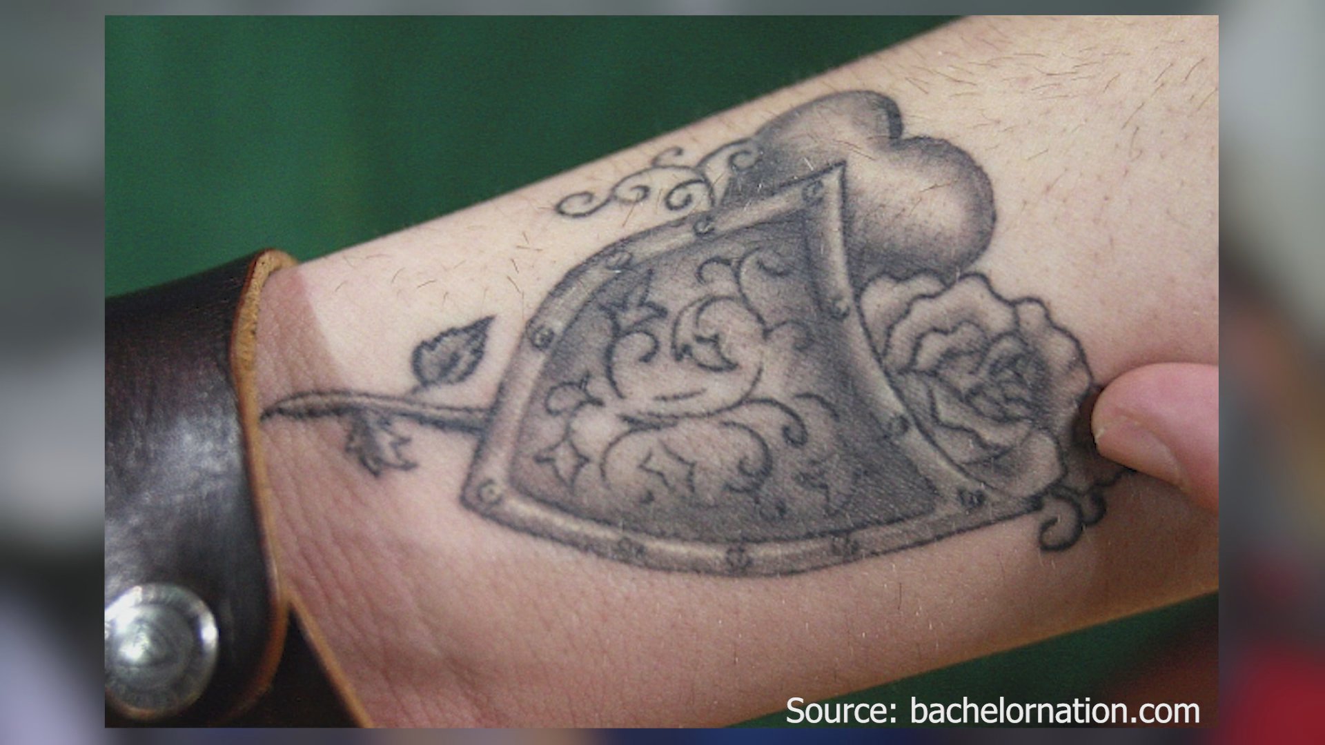 A close-up view displays a detailed black-and-grey tattoo featuring a shield, a rose, and a heart design on a person's forearm.