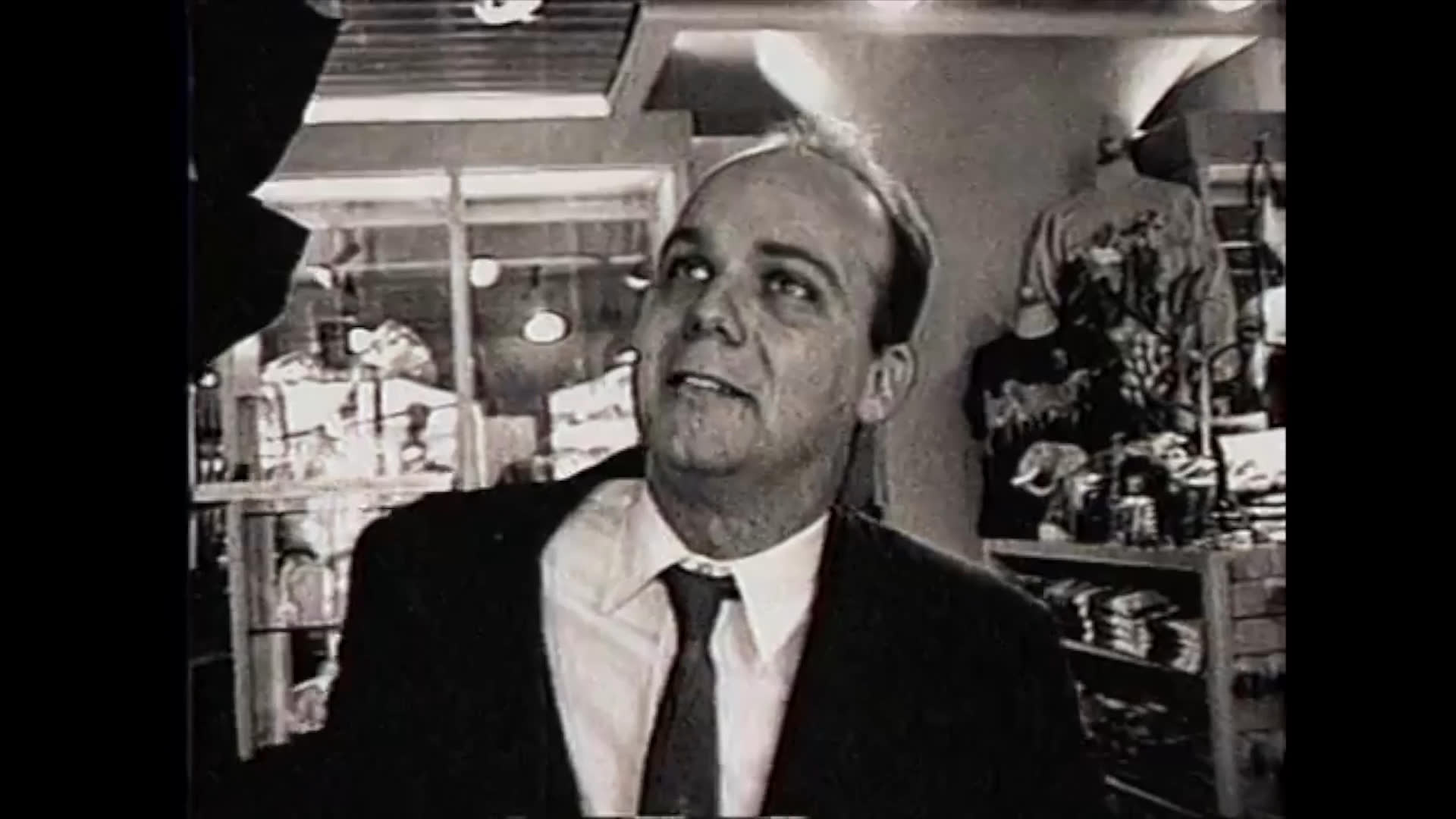 A man in a suit engages in a professional conversation with a woman inside a retail store. The scene captures their exchange within the shop environment through alternating close-up shots.