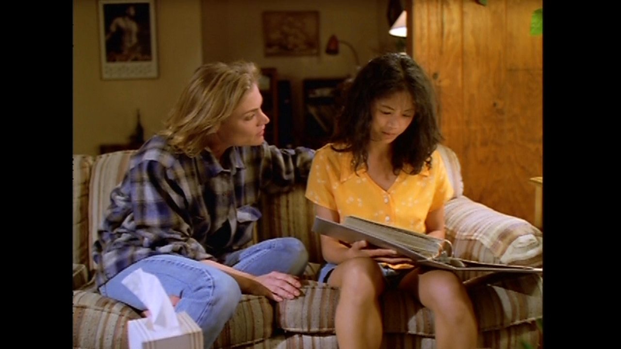 Two women sit together on a sofa, looking through a photo album while sharing an intimate and emotional moment of remembrance.