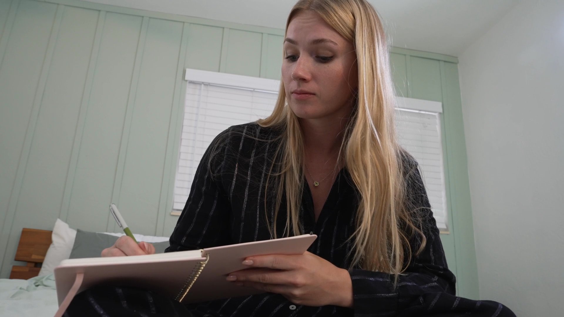 A man peeks into a room where a woman writes in a notebook, before the two transition to a kitchen setting to converse with an older woman. The individuals engage in coordinated activities and discussion within a home environment.
